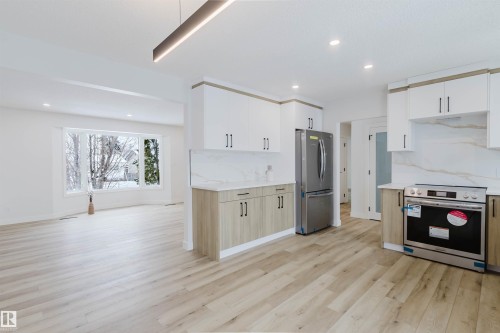 Open concept living space featuring light wood flooring, a kitchen with white and wood-toned cabinetry, stainless steel appliances, and a large window providing views of the outdoors - 11528 42 Avenue, Edmonton, AB - Indoor Photo Showing Kitchen