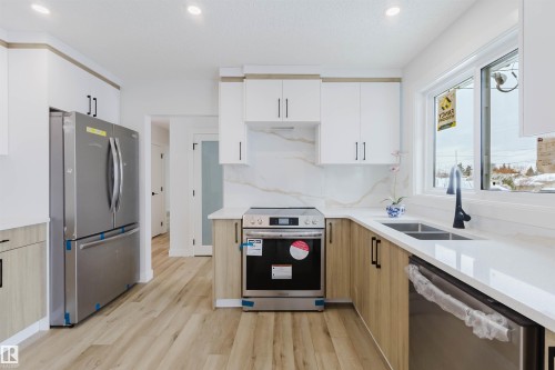 Kitchen featuring stainless steel appliances, light wood tone and white cabinetry, quartz countertops, a double basin sink, and a large window - 11528 42 Avenue, Edmonton, AB - Indoor Photo Showing Kitchen With Double Sink With Upgraded Kitchen