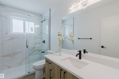 Modern bathroom featuring a glass-enclosed shower with marbled walls, a vanity with a white countertop and rectangular sink, and a large mirror - 11528 42 Avenue, Edmonton, AB - Indoor Photo Showing Bathroom