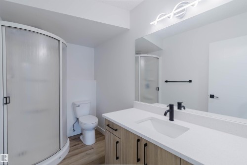 Bathroom featuring a curved shower with frosted glass, a vanity with a white countertop and dark fixtures, and wood-look flooring - 11528 42 Avenue, Edmonton, AB - Indoor Photo Showing Bathroom