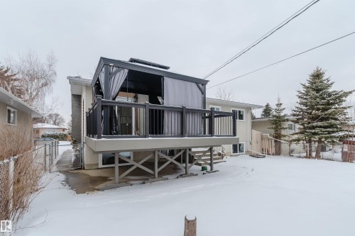 The property features a raised deck with dark railings, a privacy gazebo, and a snow-covered yard with mature evergreen trees - 11528 42 Avenue, Edmonton, AB - Outdoor
