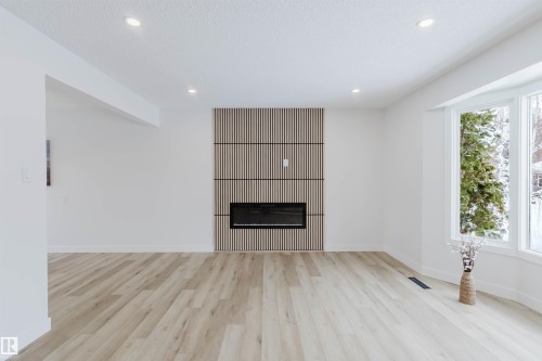 This bright living space features light-toned flooring, recessed lighting, and a prominent fireplace with a slat-panel surround - 11528 42 Avenue, Edmonton, AB - Indoor With Fireplace