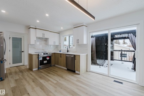 The kitchen features modern white cabinetry, light wood-look flooring, stainless steel appliances, and a marble-style backsplash - 11528 42 Avenue, Edmonton, AB - Indoor Photo Showing Kitchen