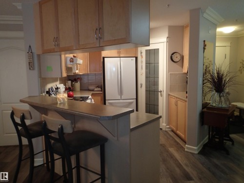 The kitchen features light-toned cabinetry, a breakfast bar, and wood-style flooring - 206 10208 120 Street, Edmonton, AB - Indoor