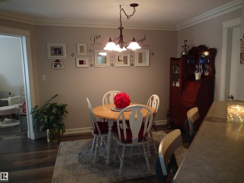 Dining area featuring crown molding, overhead lighting, a decorative wall, and neutral wood laminate flooring - 206 10208 120 Street, Edmonton, AB - Indoor Photo Showing Dining Room