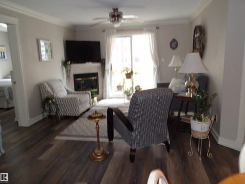 This inviting living area features hardwood style flooring, a fireplace, and a ceiling fan leading to the south facing balcony - 206 10208 120 Street, Edmonton, AB - Indoor Photo Showing Living Room With Fireplace