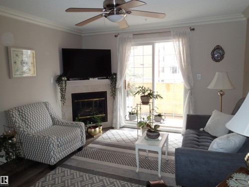 This living space features a fireplace with a light-colored mantel, a ceiling fan with integrated lighting, and a sliding glass door leading to an outdoor area - 206 10208 120 Street, Edmonton, AB - Indoor Photo Showing Living Room With Fireplace
