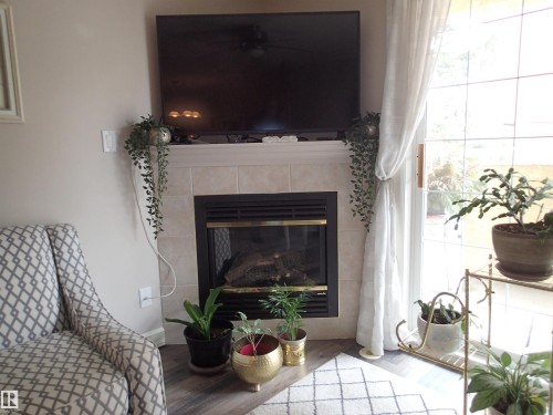 Living area featuring a fireplace with a tiled surround and hearth, light-colored walls, and flooring - 206 10208 120 Street, Edmonton, AB - Indoor Photo Showing Living Room With Fireplace