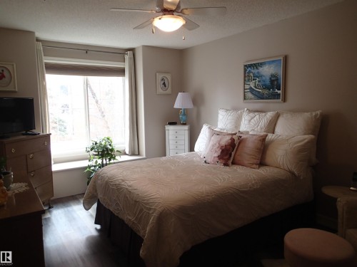 This bedroom features a window with a deep sill, a ceiling fan with integrated lighting, and wood-style flooring - 206 10208 120 Street, Edmonton, AB - Indoor Photo Showing Bedroom
