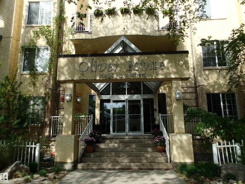 Building entrance featuring multi-story stucco exterior, a glass-enclosed main entry, and a prominent building sign - 206 10208 120 Street, Edmonton, AB - Outdoor