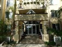 Building entrance featuring multi-story stucco exterior, a glass-enclosed main entry, and a prominent building sign - 206 10208 120 Street, Edmonton, AB  - Outdoor 
