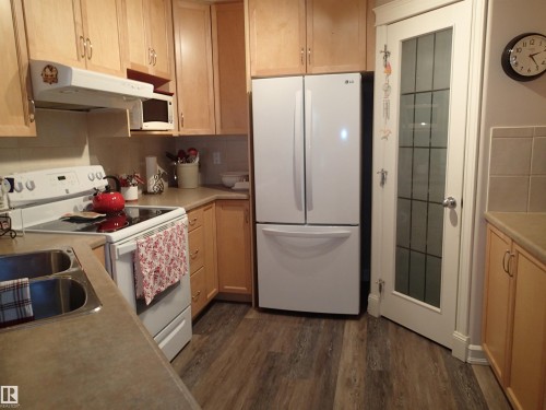 The kitchen features light wood cabinetry, a white refrigerator, and a white electric range with an microwave shelf. - 206 10208 120 Street, Edmonton, AB - Indoor Photo Showing Kitchen With Double Sink