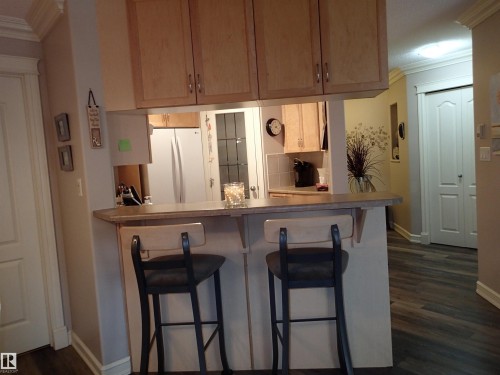 The kitchen features light wood cabinetry, a pass-through bar with counter seating. - 206 10208 120 Street, Edmonton, AB - Indoor Photo Showing Kitchen