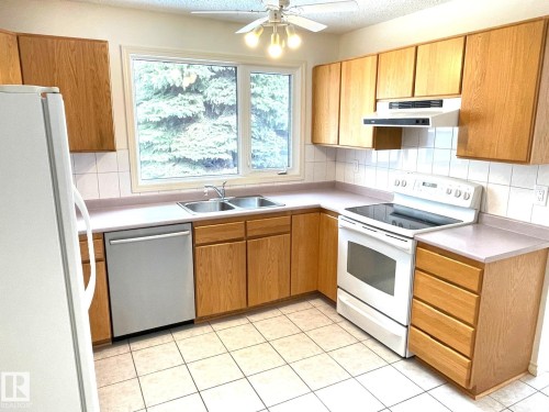 The kitchen features light-toned wooden cabinetry, light countertops, and a white tiled floor - 44 Arlington Drive, St. Albert, AB - Indoor Photo Showing Kitchen With Double Sink