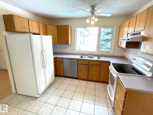 The kitchen features wood cabinetry, a double basin sink, and tile flooring - 44 Arlington Drive, St. Albert, AB - Indoor Photo Showing Kitchen With Double Sink