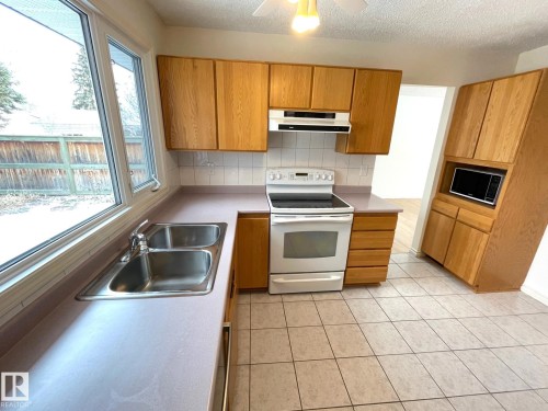 The kitchen features wood cabinetry, a double basin stainless steel sink, and tile flooring - 44 Arlington Drive, St. Albert, AB - Indoor Photo Showing Kitchen With Double Sink