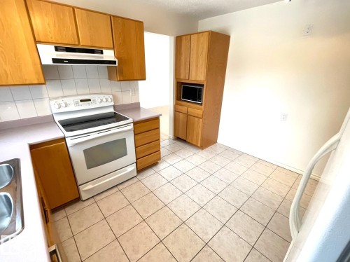 The kitchen features light wood cabinetry, white appliances including a range and microwave, and a white tiled backsplash - 44 Arlington Drive, St. Albert, AB - Indoor Photo Showing Kitchen