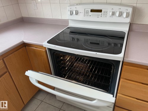 Kitchen featuring a white electric range with a glass cooktop and an open oven, light-colored countertops, and wooden cabinetry - 44 Arlington Drive, St. Albert, AB - Indoor Photo Showing Kitchen