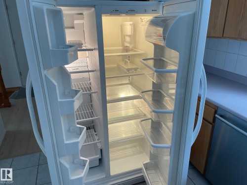 The kitchen features a side-by-side refrigerator with interior lighting, clear door bins, and adjustable shelving - 44 Arlington Drive, St. Albert, AB - 