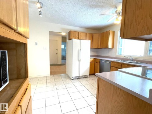 The kitchen features white tiled flooring, a double basin sink beneath a window, and light wood cabinetry throughout - 44 Arlington Drive, St. Albert, AB - Indoor Photo Showing Kitchen With Double Sink