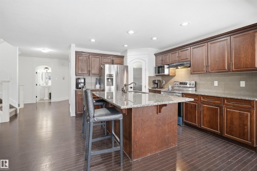 The kitchen features dark wood cabinetry, stainless steel appliances, and a central island with a granite countertop - 469 Ainslie Crescent Sw, Edmonton, AB - Indoor Photo Showing Kitchen With Upgraded Kitchen