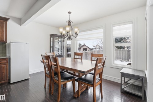 Dining area featuring dark wood flooring, a decorative chandelier, and large windows providing natural illumination - 469 Ainslie Crescent Sw, Edmonton, AB - Indoor Photo Showing Dining Room