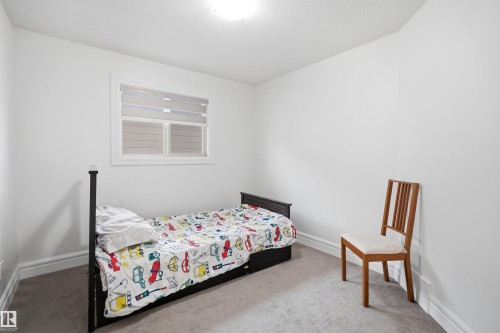 This room features light-colored walls and carpeting, a window with blinds, and white trim along the base of the walls - 469 Ainslie Crescent Sw, Edmonton, AB - Indoor Photo Showing Bedroom
