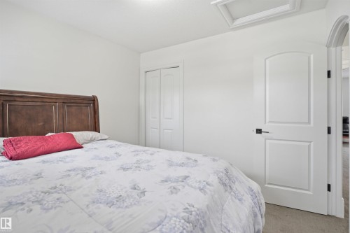 This room features light-colored walls and carpeted flooring, with a dark wooden headboard providing a contrast - 469 Ainslie Crescent Sw, Edmonton, AB - Indoor Photo Showing Bedroom