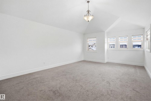 The room features a vaulted ceiling with a decorative chandelier, light gray carpeting, and multiple windows with blinds providing natural light - 469 Ainslie Crescent Sw, Edmonton, AB - Indoor Photo Showing Other Room