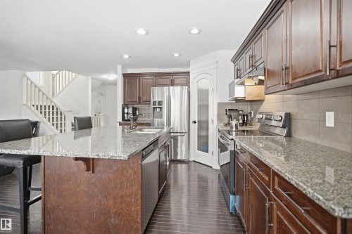 The kitchen features granite countertops, dark wood cabinetry, and stainless steel appliances - 469 Ainslie Crescent Sw, Edmonton, AB - Indoor Photo Showing Kitchen With Upgraded Kitchen