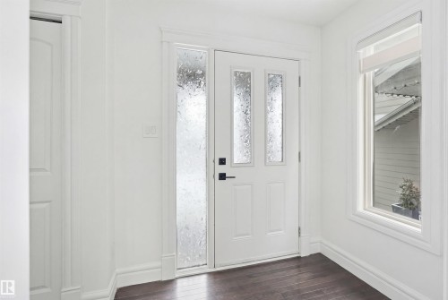 The property features a white paneled front door with decorative glass inserts, complemented by a large sidelight with textured glass - 469 Ainslie Crescent Sw, Edmonton, AB - Indoor Photo Showing Other Room