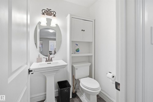 Bathroom featuring a white pedestal sink with a mirror and vanity lighting, a toilet, and built-in storage shelving - 469 Ainslie Crescent Sw, Edmonton, AB - Indoor