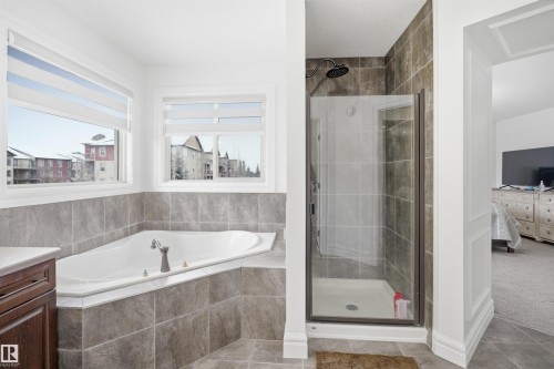 Bathroom featuring a built-in bathtub with tiled surround, a tiled walk-in shower with a glass door, and two windows with blinds - 469 Ainslie Crescent Sw, Edmonton, AB - Indoor Photo Showing Bathroom