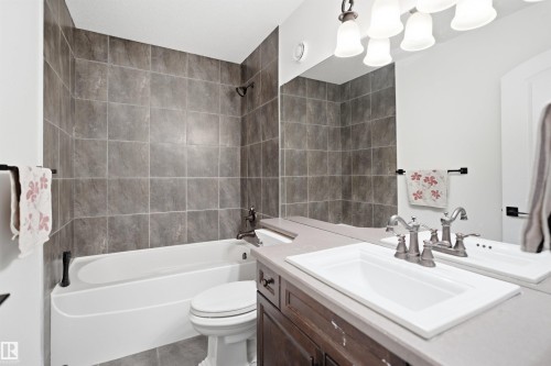 Bathroom featuring a white bathtub with a tiled shower surround, a vanity with a white rectangular sink, and a large mirror - 469 Ainslie Crescent Sw, Edmonton, AB - Indoor Photo Showing Bathroom
