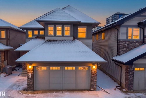 The property features an attached double garage with window panels and exterior lighting, a stone facade, and a snow-covered roof - 469 Ainslie Crescent Sw, Edmonton, AB - Outdoor