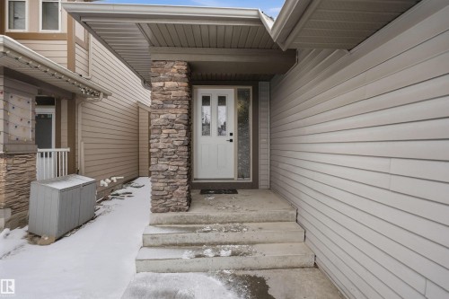 The property features a white paneled front door with decorative glass inserts, complemented by a stone-clad pillar and concrete steps - 469 Ainslie Crescent Sw, Edmonton, AB - Outdoor With Exterior
