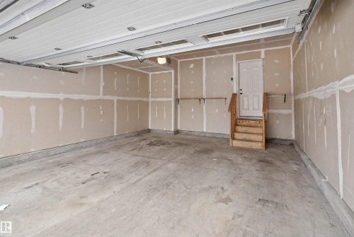 The DOUBLE CAR garage features a concrete floor, a white overhead garage door, a side door with wooden stairs, and a wall-mounted light fixture - 469 Ainslie Crescent Sw, Edmonton, AB - Indoor Photo Showing Garage