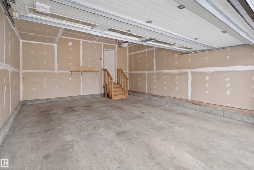 Spacious garage with a concrete floor, an overhead door, and a wooden staircase providing access to the interior - 469 Ainslie Crescent Sw, Edmonton, AB - Indoor Photo Showing Garage