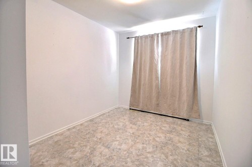 This room features white walls, a light-colored flooring, and a window dressed with a neutral-toned curtain - 5109 49 Avenue, Andrew, AB - Indoor Photo Showing Other Room