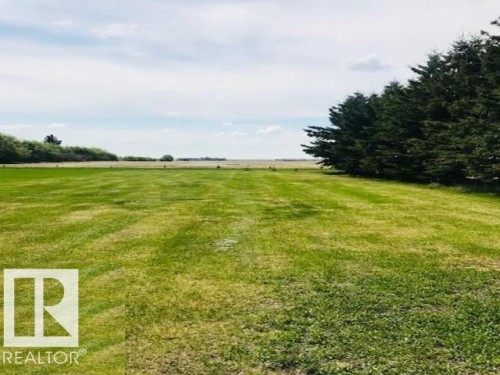 Expansive, well-maintained lawn with mature evergreen trees bordering one side, offering an open view of the surrounding landscape - 5109 49 Avenue, Andrew, AB - Outdoor With View