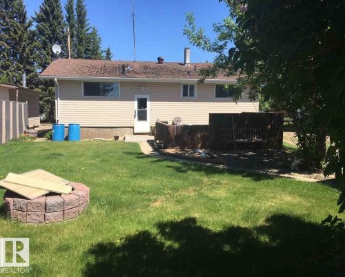 The property offers a backyard with a lawn, a brick-built fire pit, and a wooden deck area - 5109 49 Avenue, Andrew, AB - Outdoor