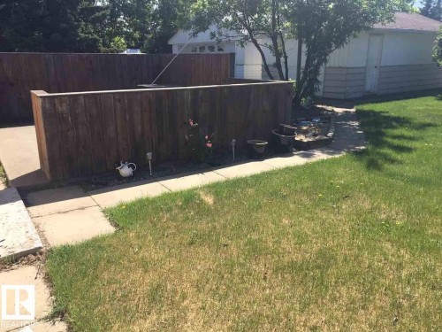 The property features a fenced yard with a lawn, a paved patio area, and a detached garage - 5109 49 Avenue, Andrew, AB - Outdoor