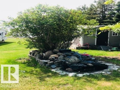 The property features a well-maintained lawn, a decorative pond with natural stone accents, and a mature shrub - 5109 49 Avenue, Andrew, AB - Outdoor