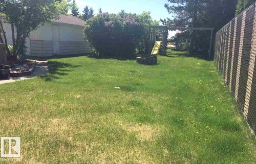 The property features an expansive green lawn, a white detached garage, and mature bushes - 5109 49 Avenue, Andrew, AB - Outdoor