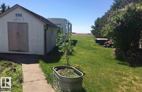 The property features a green lawn, a detached shed with a concrete walkway, and mature trees lining the property boundary - 5109 49 Avenue, Andrew, AB - Outdoor