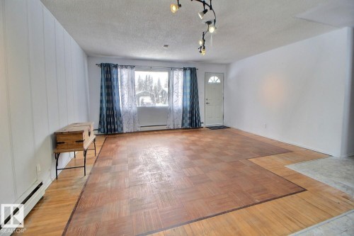 The living area features a combination of parquet and light wood flooring, a window with curtains, and a track lighting fixture - 5109 49 Avenue, Andrew, AB - Indoor Photo Showing Other Room