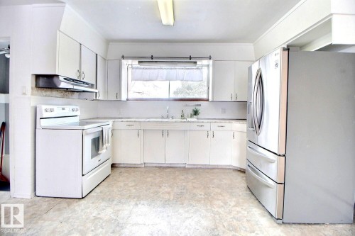 The kitchen features white cabinetry, a white electric range, and a stainless steel refrigerator - 5109 49 Avenue, Andrew, AB - Indoor Photo Showing Kitchen