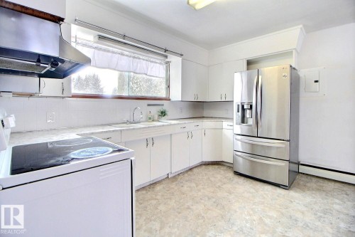 The kitchen features white cabinetry, a stainless steel refrigerator, and a window above the sink - 5109 49 Avenue, Andrew, AB - Indoor Photo Showing Kitchen