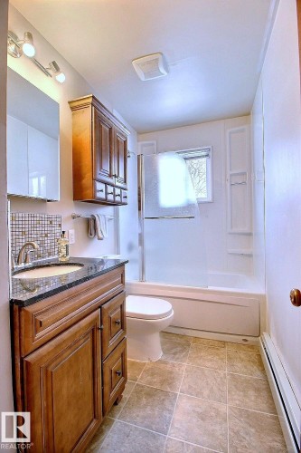 Bathroom featuring a wood vanity with a granite countertop, a bathtub with a shower enclosure, and tiled flooring - 5109 49 Avenue, Andrew, AB - Indoor Photo Showing Bathroom