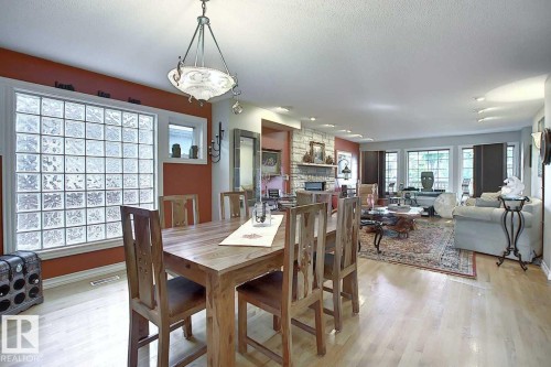 Spacious open-concept living area featuring light wood flooring, a dining area with a wood table and chairs, and a living room with a large area rug and a stone fireplace - 11126 52 Street, Edmonton, AB - Indoor Photo Showing Dining Room
